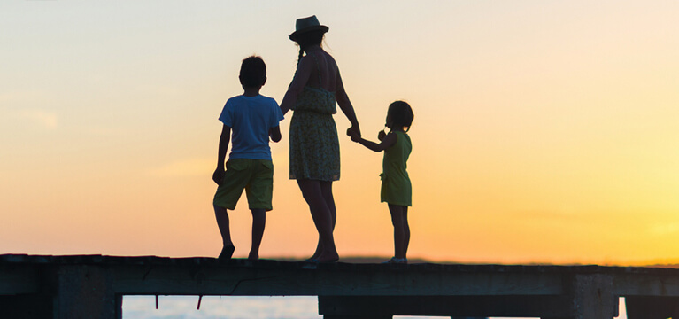Mother and two children standing on a dock at sunset